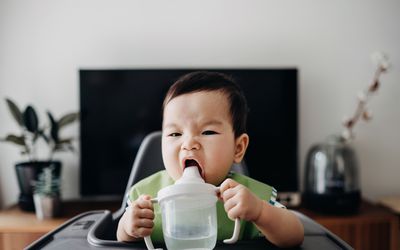 可爱的婴儿饮用水从高脚椅子上的sp杯