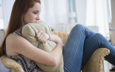 a young woman looking sad, holding a pillow on a chair