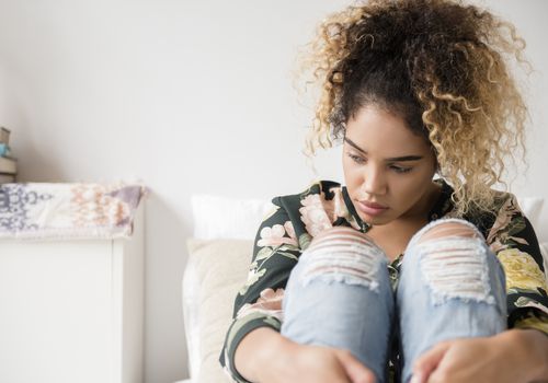 Pensive young woman sitting on a bed